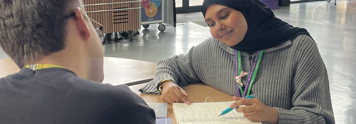 Safa working at a table with a notebook and pen facing a colleague