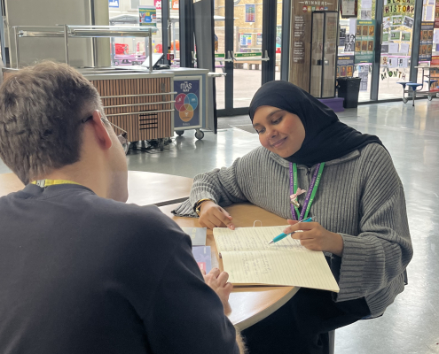Safa working at a table with a notebook and pen facing a colleague