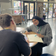 Safa working at a table with a notebook and pen facing a colleague